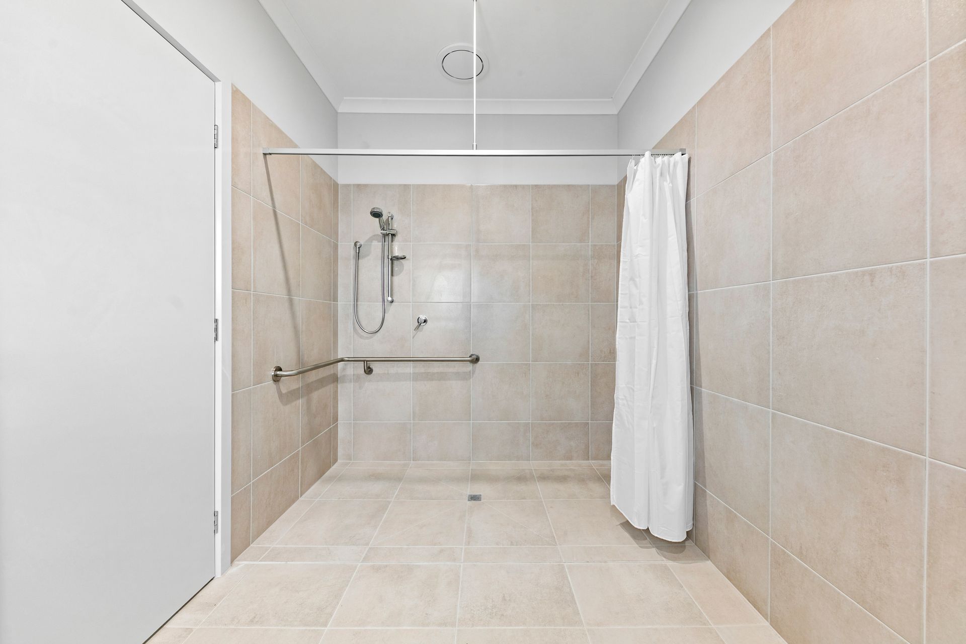 A step-free shower with a grab rail and a curtain.