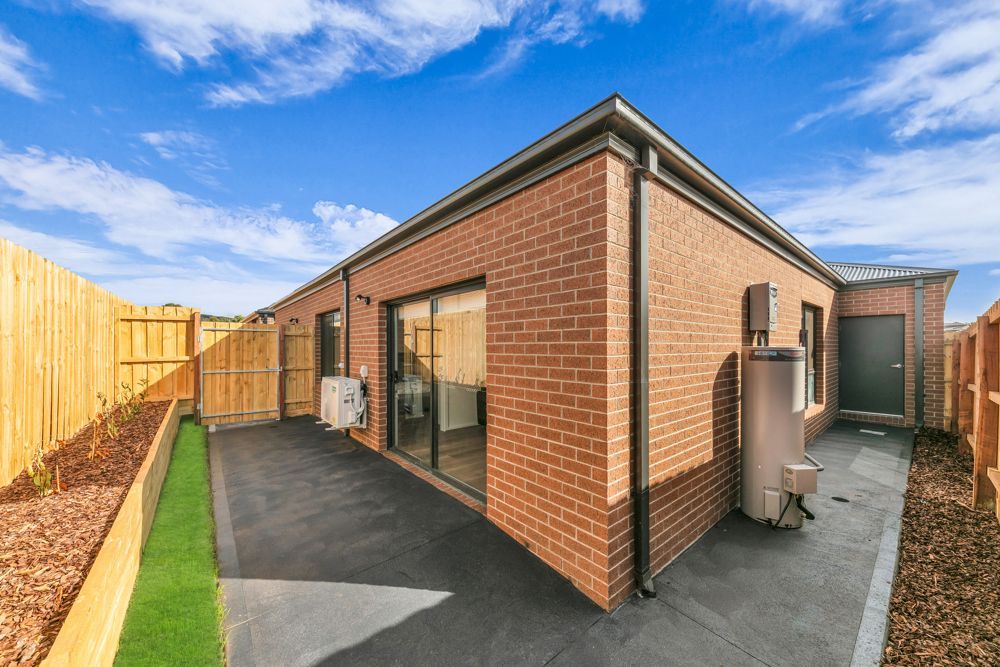 The side of the home: a brick house with a paved path and fenced yard.