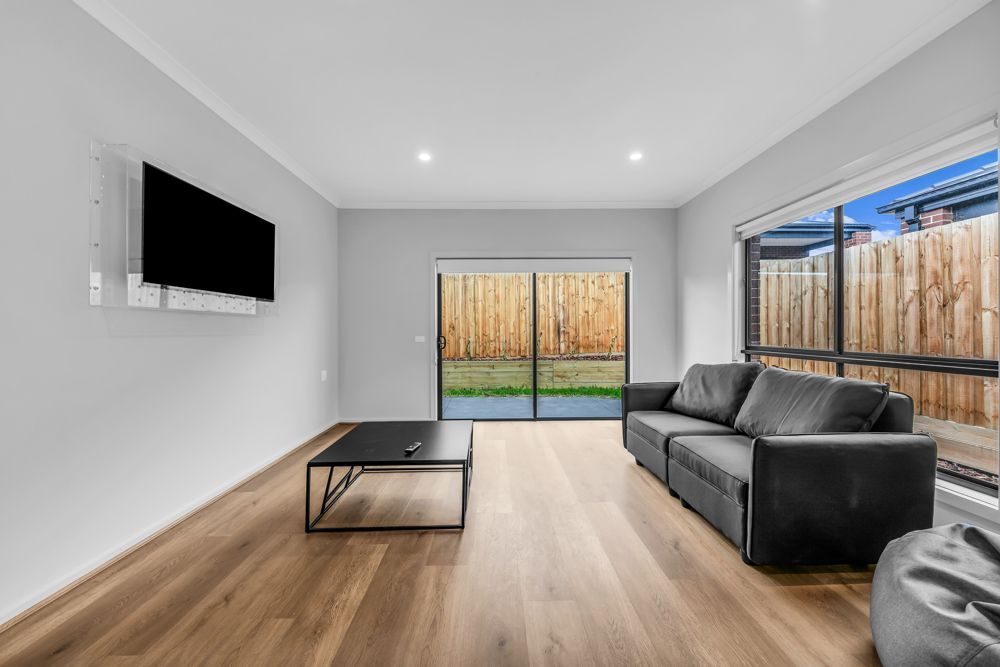 The lounge, with a sofa, wall-mounted TV and a sliding door to the yard.